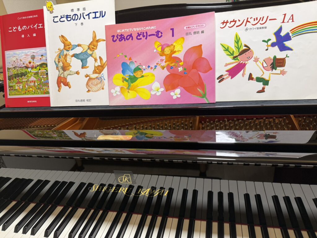 グランドピアノ(Shigeru Kawai)の鍵盤と譜面台に並ぶ『こどものバイエル』や『ぴあのどりーむ』などの子供向けピアノ教材